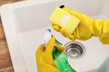 Beyaz lavaboyu süngerle temizleyen kadın, kabartma tozu ve sprey, yakın çekim.