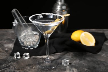 Bir bardak zeytinli, buzlu ve koyu arkaplanda limonlu martini.