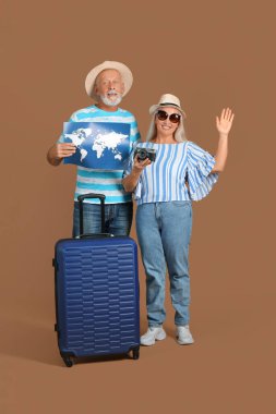 Çantalı yaşlı çift, dünya haritası ve kahverengi arka planda kamera.