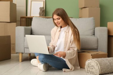 Yeni dairede dizüstü bilgisayarıyla yerde oturan genç bir kadın. Taşınma konsepti