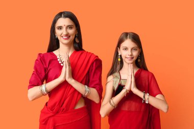 Anne ve kızı sari 'de turuncu arka planda dua ediyorlar. Divaly kutlaması