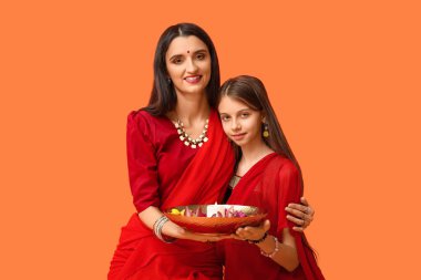 Anne ve kızı sari içinde ellerinde mum ve turuncu arka planda çiçekler tutuyorlar. Divaly kutlaması