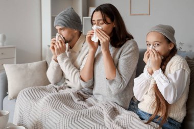 Evde kanepede hapşıran peçeteli hasta bir aile.