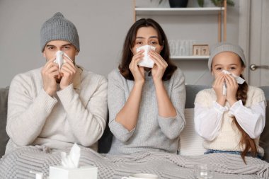 Evde kanepede hapşıran peçeteli hasta bir aile.