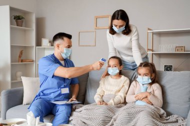 Doktor evde hasta küçük bir kızın ateşini ölçüyor.