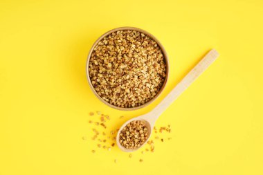 Sarı zemin üzerinde çiğ karabuğday taneleri olan kase