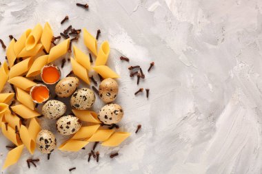 Pişmemiş makarna, karanfil ve arkaplanda çiğ bıldırcın yumurtası.