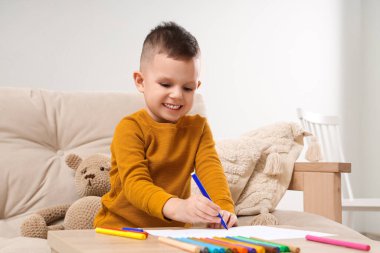 Evdeki masada keçeli kalemlerle çizen sevimli küçük çocuk.