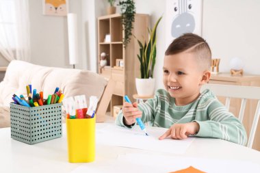 Evdeki masada keçeli kalemle çizen komik küçük çocuk.