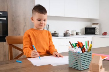 Mutfaktaki masasında keçeli kalemlerle çizen sevimli küçük çocuk.