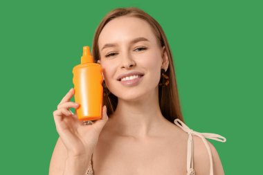 Yeşil arka planda güneş kremi şişesi olan güzel, genç ve mutlu bir kadın.