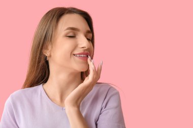 Güzel genç bir kadın pembe arka planda dudaklarına dokunuyor.