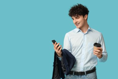 Cep telefonu ve mavi arka planda bir fincan kahve olan yakışıklı bir iş adamı.
