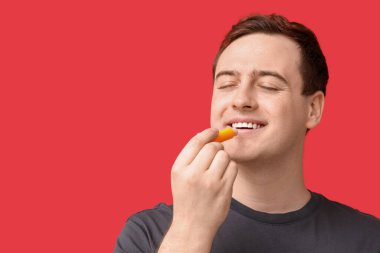 Kırmızı arka planda dudak merhemi olan yakışıklı bir genç.