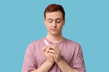 Mavi arka planda dudak merhemi olan düşünceli genç bir adam.