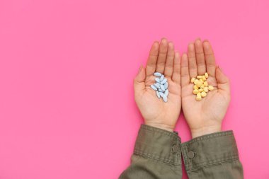 Pembe arka planda farklı hapları olan kadın elleri.