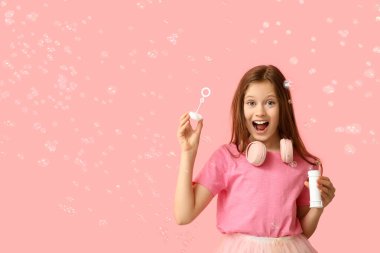 Mutlu kız pembe arka planda sabun köpükleri üflüyor.