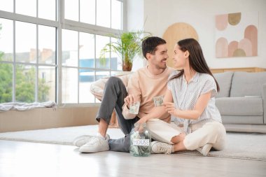 Genç çift evde kavanoza para koyuyor.