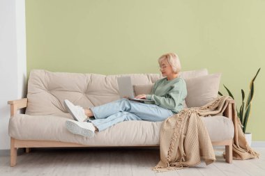 Yeşil duvarın yanındaki koltukta dizüstü bilgisayarı olan orta yaşlı bir kadın.