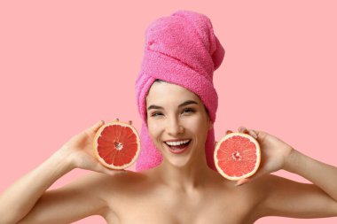 Pembe arka planda greyfurtu olan güzel genç bir kadın.