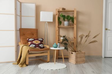 Kol sandalyesi, ekose, katlanan ekran, kahve masası ve otlu sepet oturma odasında.