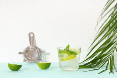 Kokteyl süzgeci ve tropikal yapraklı bir bardak taze mojito beyaz arka planda mavi masada.