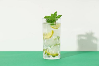 Beyaz arka plana karşı yeşil masada bir bardak taze mojito.
