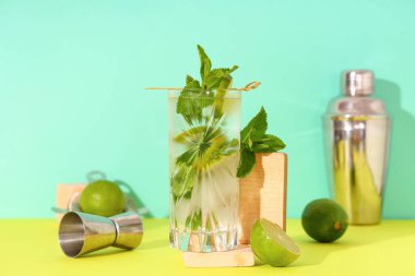 Turkuaz arka planda sarı masada jigger ile bir bardak taze mojito.