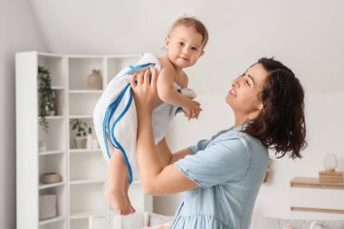 Anne, evde banyo yaptıktan sonra küçük bebeğini yumuşak havluyla gezdiriyor.