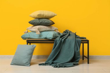 Sarı duvarın yanındaki bankta ekoseli yastık yığını.