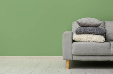 Yeşil duvarın yanındaki gri kanepede yastıklar.