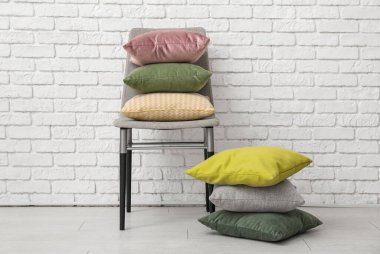 Odadaki beyaz tuğla duvarın yanındaki sandalyeye yığılmış yastıklar.