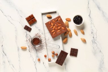 Badem fıstıklı çikolata, fındık ve beyaz arka planda kakao tozu.