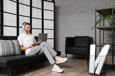 Ofisteki koltukta dizüstü bilgisayar kullanan kulaklıklı genç sakallı adam.