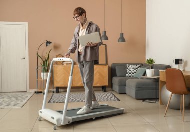 Ofiste koşu bandında dizüstü bilgisayar eğitimi alan genç bir adam.