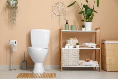 Tuvalette bej duvarın yanında klozet ve raf üniteleri var.