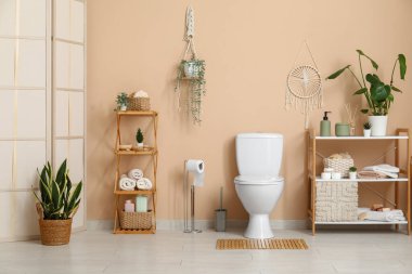 Tuvalette bej duvarın yanında klozet ve raf üniteleri var.