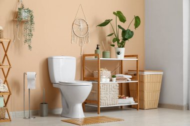 Tuvalette bej duvarın yanında klozet ve raf üniteleri var.