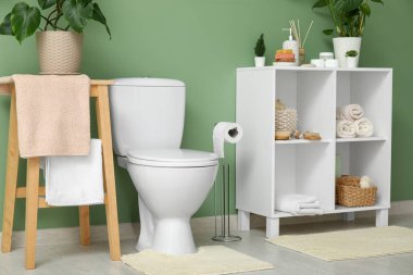 Tuvalette yeşil duvarın yanında klozet ve raf üniteleri var.