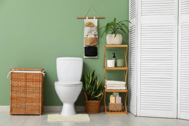 Tuvaletin içinde klozet, raf ünitesi, çamaşır sepeti ve yeşil duvarın yanında organizatör var.
