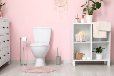 Tuvalet klozeti, raf ünitesi ve çekmeceler tuvaletteki pembe duvarın yanında.