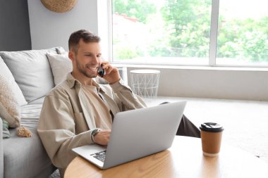 Bilgisayarlı yakışıklı adam evde cep telefonuyla konuşuyor.