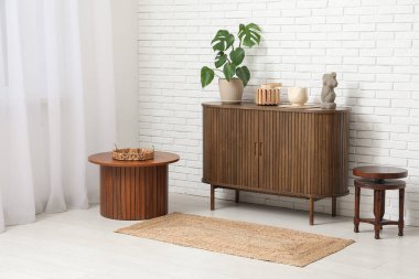 Beyaz tuğla duvarın yanında bitki, dekor ve kahve sehpaları olan şık çekmeceler.