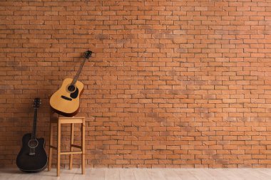 Kahverengi duvarın yanındaki sandalyede farklı gitarlar.