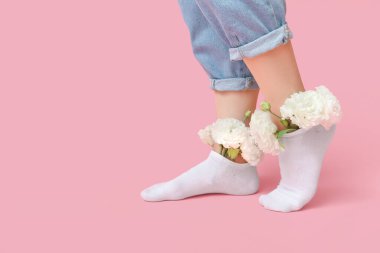 Pembe arka planda östoma çiçekleri olan beyaz çoraplı genç kadın bacakları.