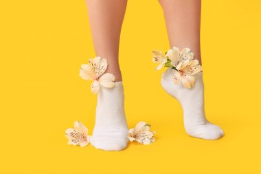 Beyaz çoraplı, sarı arka planda merhem çiçekleri olan genç bir kadının bacakları.