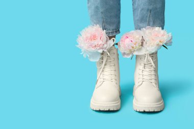 Mavi arka planda şakayık çiçekleri olan çizmeli genç bir kadının bacakları.