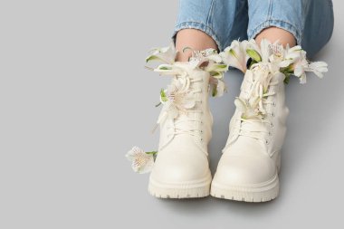 Gri arka planda alstromerya çiçekleri olan çizmeli genç kadın bacakları.