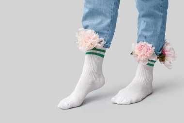 Gri arka planda şakayık çiçekleri olan beyaz çoraplı genç kadın bacakları.