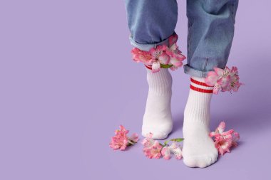 Beyaz çoraplı, leylak arkaplanda alstromerya çiçekleri olan genç kadın bacakları.